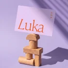 Luka minimalistisch geboortekaartje met de naam groot in een elegant oranje serif-lettertype op zacht lila, datum klein rechtsboven